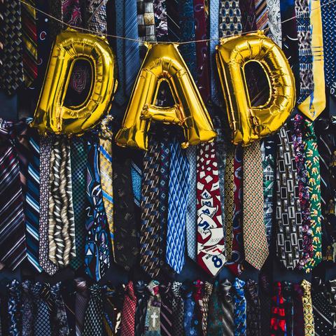 Gold balloons spelling out DAD, on a background of funky pattern ties all hung up. Two rows of around 40 ties.