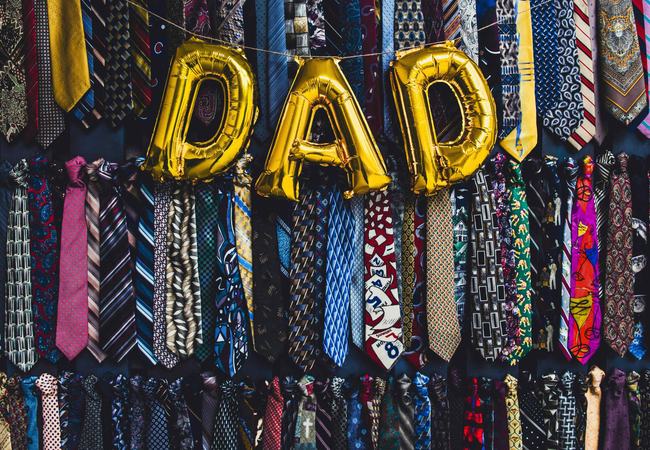 Gold balloons spelling out DAD, on a background of funky pattern ties all hung up. Two rows of around 40 ties.