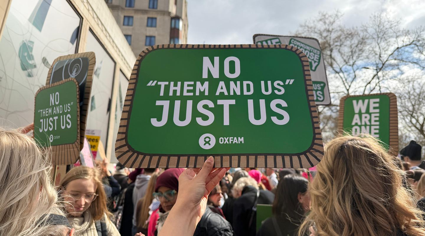 Hand holding a sign up at a march. The sign says 'There is no them and us, just us'