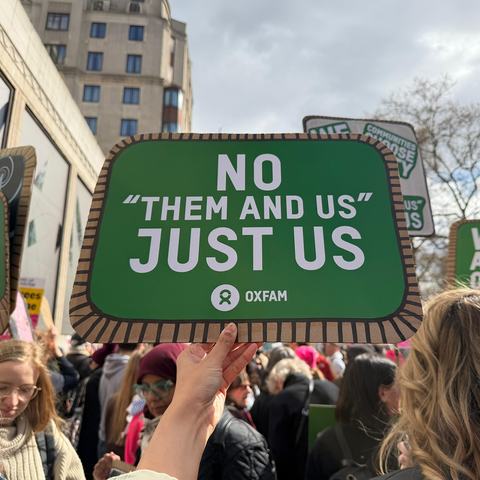 Hand holding a sign up at a march. The sign says 'There is no them and us, just us'