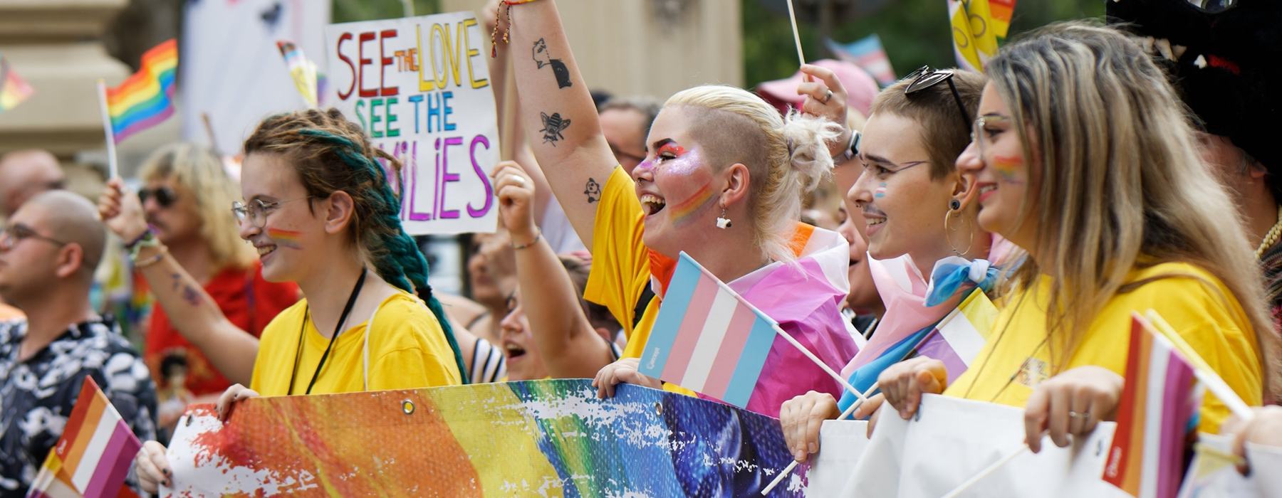 A group of young people at a Pride march holding LGBTQIA+ flags and banners