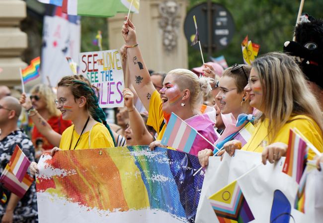 A group of young people at a Pride march holding LGBTQIA+ flags and banners