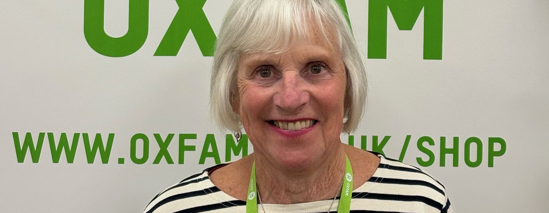 Photo of Sandra smiling in front of an Oxfam sign