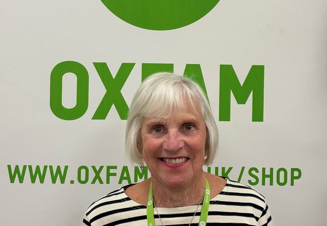 Photo of Sandra smiling in front of an Oxfam sign