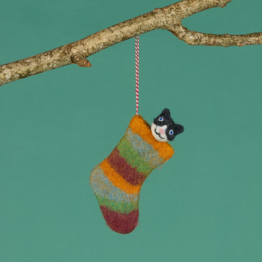 Black and white felt cat with its head popping out of a striped felt Christmas stocking, hanging from a tree branch