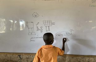 A student in a school in Ghana draws a solar panel on a whiteboard.
