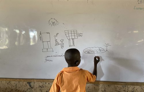 A student in a school in Ghana draws a solar panel on a whiteboard.