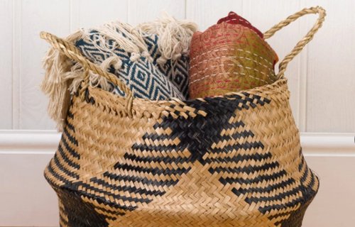 A seagrass basket filled with rolled blankets and rugs