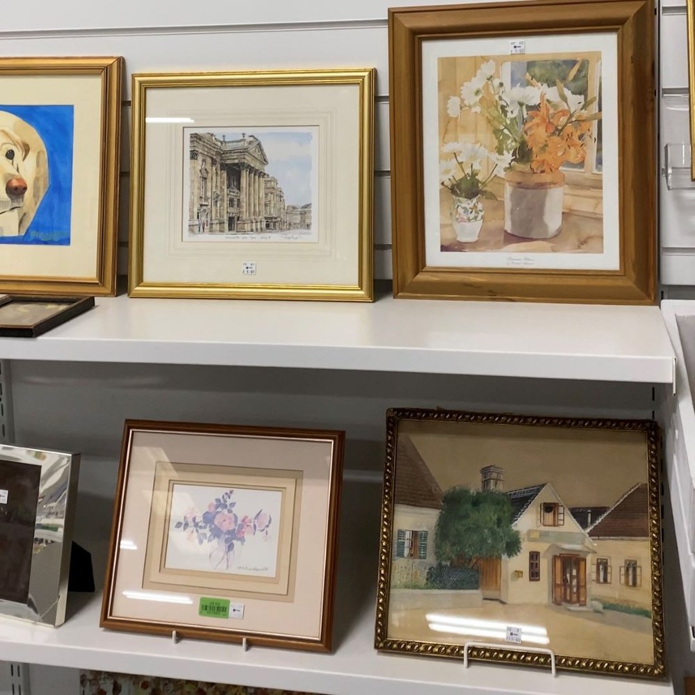 Wall of second hand artwork for sale in Oxfam charity shop