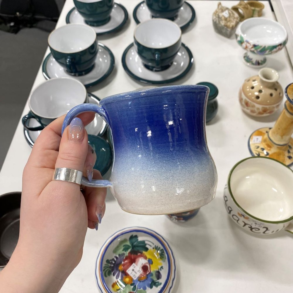 a hand holding a blue second hand mug found in an Oxfam shop