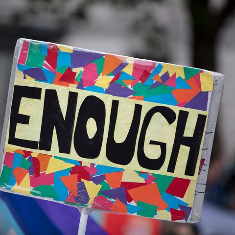 A rainbow coloured protest sign that says 'enough' on it.