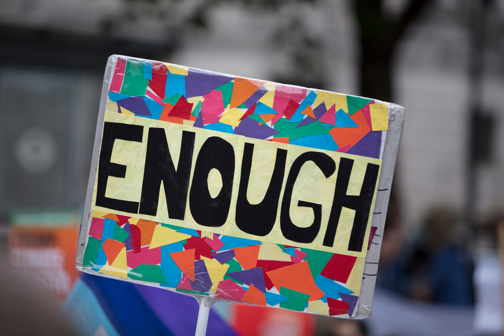 A rainbow coloured protest sign that says 'enough' on it.