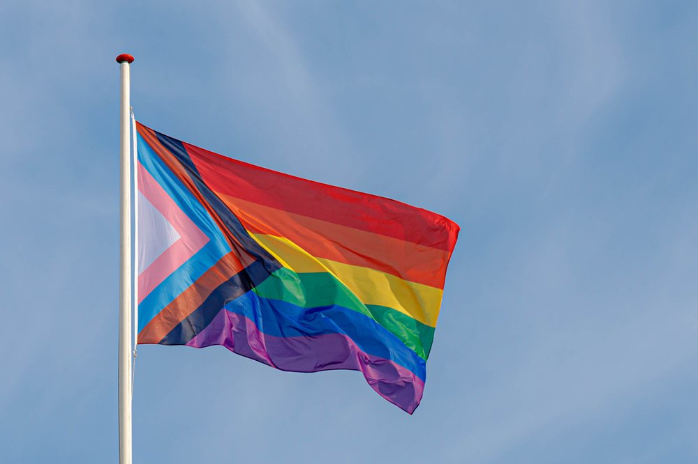 A rainbow progress flag flying with blue sky in the background