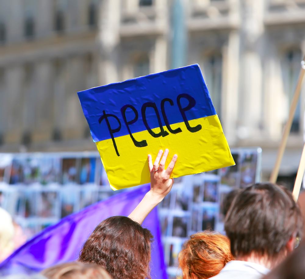 A sign with a Ukraine flag and Peace written on it held up in a crowd