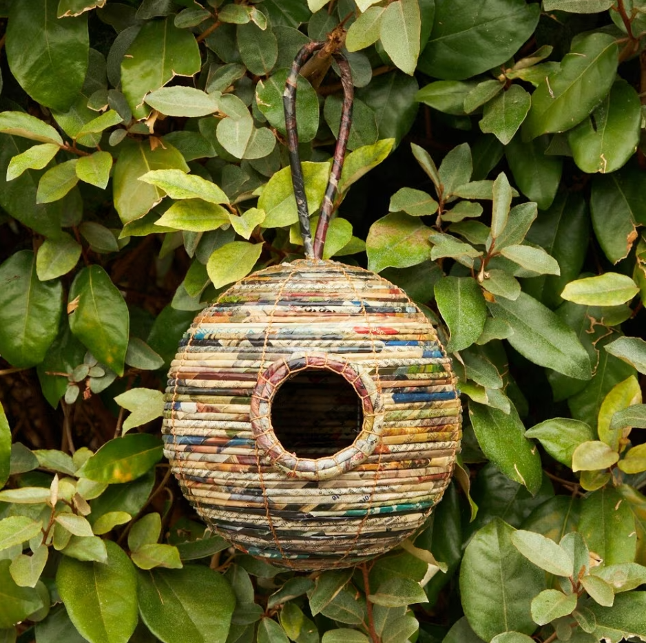 Round bird house made from recycled paper, hanging from a branch