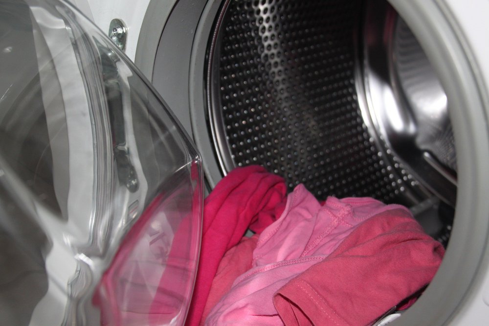 Red and pink clothes hanging out of a washing machine with its door open