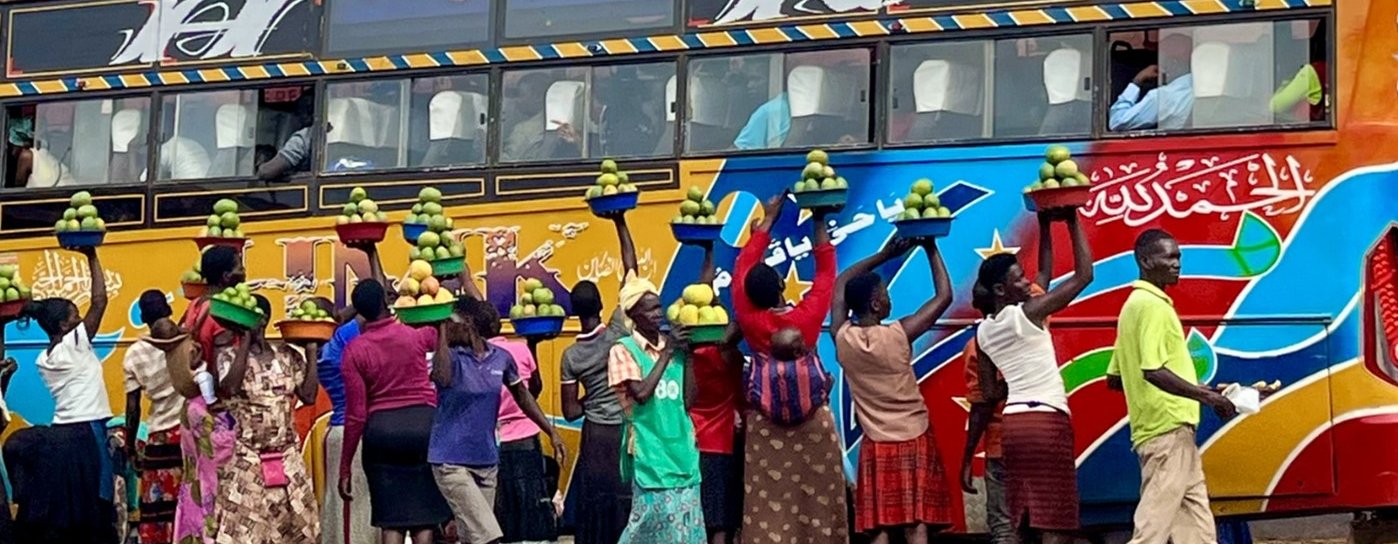 Women stood beside a colourful bus holding up baskets of mangos to sell to the passengers.