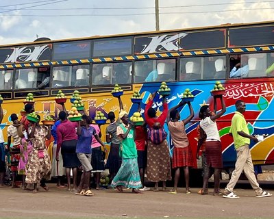 Women stood beside a colourful bus holding up baskets of mangos to sell to the passengers.