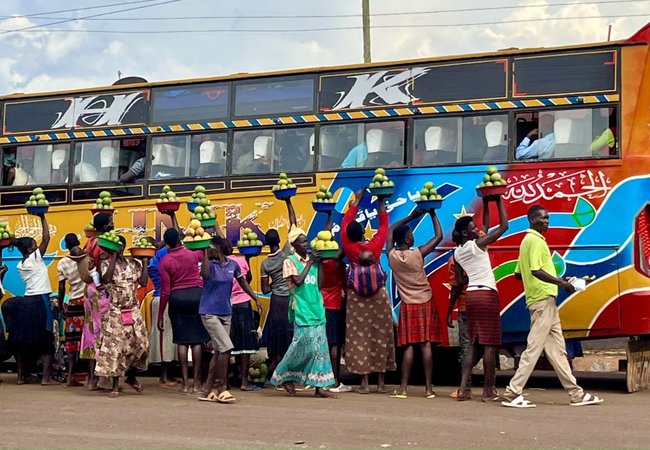 Women stood beside a colourful bus holding up baskets of mangos to sell to the passengers.